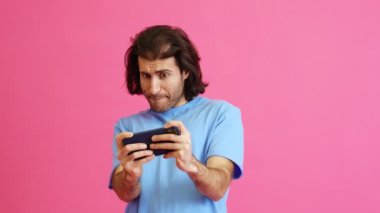 Hevesli bir adam telefonda oynuyor ve pembe bir stüdyoda dururken kaybettiği için üzülüyor.
