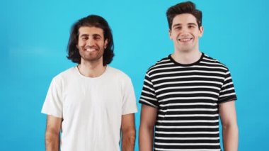 Mavi bir stüdyoda duran tişörtlü iki adam.