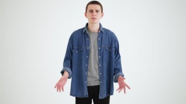 Gri bir stüdyoda dikilirken kafasını yanlış anlayan kısa saçlı üzgün adam.