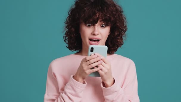 Mulher Surpresa Digitando Algo Telefone Segurando Suas Mãos Estúdio Azul — Vídeo de Stock