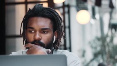 Kulaklıklı, düşünen Afro-Amerikan bir adam sokakta otururken bilgisayarını kullanıyor.