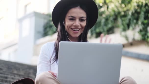 Positiv Ung Kvinna Som Bär Trådbundna Hörlurar Viftar Med Handen — Stockvideo