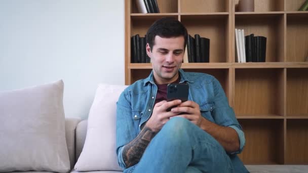 Pleased Dreaming Man Using His Smartphone While Sitting Sofa Apartments — Stock Video