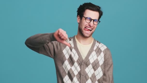 スタジオで舌を出しながら親指ダウンジェスチャーを示す眼鏡をかけた不満を抱えた男 — ストック動画