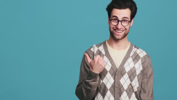 Usmívající Muž Ukazuje Prst Stranu Zatímco Stojí Modrém Studiu — Stock video