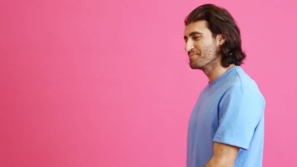 ピンクのスタジオでカメラに手を振って長い髪を歩く笑顔の男 — ストック動画