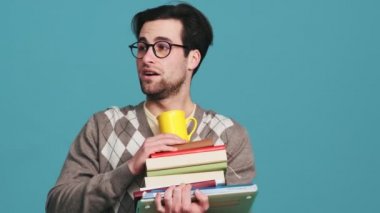The surprised man abruptly getting-up with a stack of books looking around and gradually sitting-down in them while leaving the frame in the studio