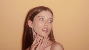 A lovely young half-naked woman is posing to the camera while doing secret gesture standing isolated over a beige background in the studio