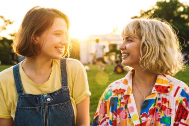 Yaz parkında dinlenirken gülümseyen ve birbirine bakan iki kadının görüntüsü.
