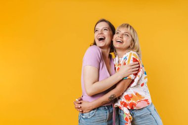 Sarı arka planda izole edilmiş, sarılıp, başka tarafa bakan, yaz kıyafetleri giyen iki güzel kız arkadaşın portresi.