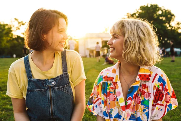 Image of happy two women laughing and looking at each other while resting in summer park