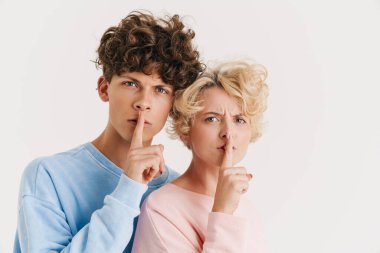 Beyaz arka planda izole edilmiş sessizlik jesti gösteren ciddi bir çiftin görüntüsü.