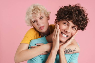 Pembe arka planda izole edilmiş tişört giyen, sarılan ve eğlenen iki genç.