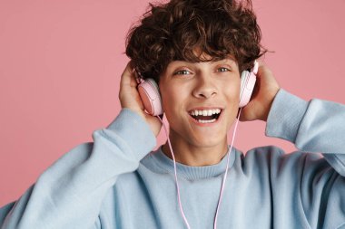 Pembe arka planda kulaklığı ile müzik dinleyen çekici bir genci yakından çek.