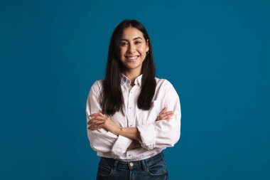 Mutlu güzel Asyalı kız gülümsüyor ve mavi arka planda izole edilmiş kameraya bakıyor.