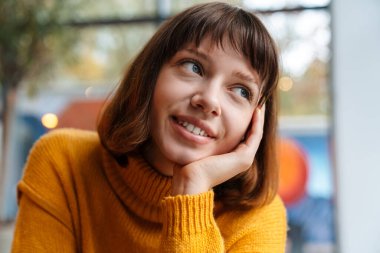 Mutlu kızıl saçlı beyaz kız içeride otururken gülümsüyor ve yan bakıyor.