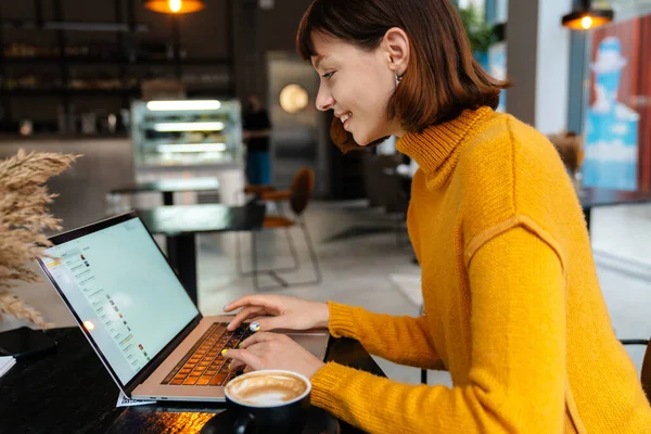 Glückliches Rothaariges Mädchen Trinkt Kaffee Und Arbeitet Mit Laptop Café — Stockfoto