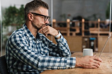 Masada dizüstü bilgisayarla çalışan tıraşsız bir adam.