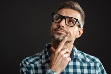 Tıraşsız, kara gözlüklü, siyah arka planda yalnız poz veren ve yan bakan bir adam.