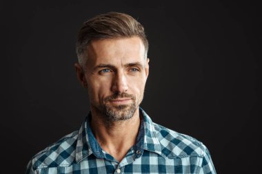 Gri duvar arkasında yalnız poz veren yakışıklı, ciddi, gri saçlı bir adamın fotoğrafı.