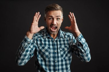 Şok olmuş traşsız adam siyah arka planda kameraya poz veriyor ve bağırıyor.