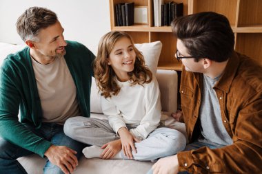 Mutlu beyaz eşcinsel çift evde kızlarıyla gülümsüyor ve konuşuyorlar.