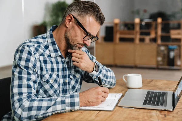 Hombre Gris Enfocado Escribiendo Notas Mientras Trabaja Con Ordenador Portátil — Foto de Stock