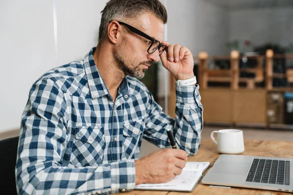 Uomo Grigio Focalizzato Annotare Note Mentre Lavora Con Computer Portatile — Foto Stock