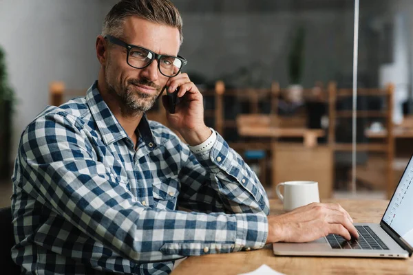 Homem Cinza Satisfeito Falando Telefone Celular Enquanto Trabalhava Com Laptop — Fotografia de Stock