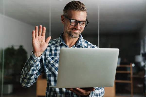 Sonriente Hombre Guapo Agitando Mano Mientras Trabaja Con Ordenador Portátil — Foto de Stock