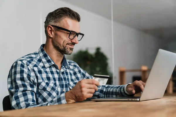 Homem Não Barbeado Satisfeito Usando Cartão Crédito Enquanto Trabalhava Com — Fotografia de Stock
