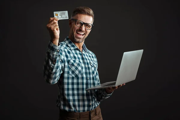 戴着眼镜 头戴墨镜 头戴手提电脑 头戴信用卡 背景为黑色的英俊而兴奋的男人 — 图库照片