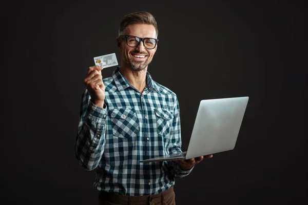 相貌俊俏 面带微笑的男人 头戴眼镜 头戴笔记本电脑 头戴信用卡 背景是黑色的 — 图库照片