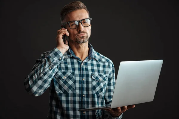 Homem Sério Óculos Segurando Laptop Falando Celular Isolado Sobre Fundo — Fotografia de Stock