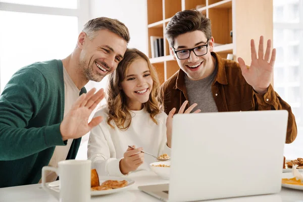 幸せなゲイのカップルと養子にビデオ通話でラップトップコンピュータ経由で自宅で 手を振って朝食中 — ストック写真