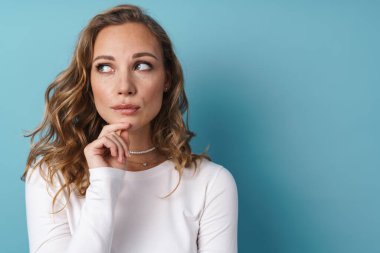 Sarışın şaşkın kadın mavi duvarın üzerinde yalnız poz veriyor ve yan bakıyor.