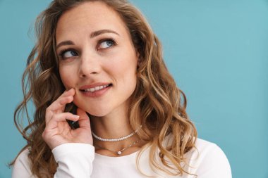 Sarışın genç beyaz kadın gülümsüyor ve mavi duvarın üzerinden yukarıya bakıyor.