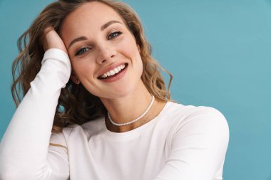 Sarışın genç kadın gülümsüyor ve mavi duvarın üzerinden izole edilmiş kameraya bakıyor.