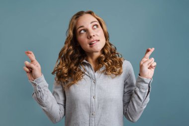 Güzel sarışın kızın şans dilemek için mavi arka planda poz verdiğini düşünmek.