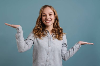 Neşeli genç kız avuçlarında kopya alanı sunuyor. Mavi arka planda izole edilmiş.