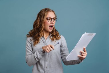 Şok olmuş gözlüklü güzel kız mavi arka planda izole edilmiş bir panoyla poz veriyor.