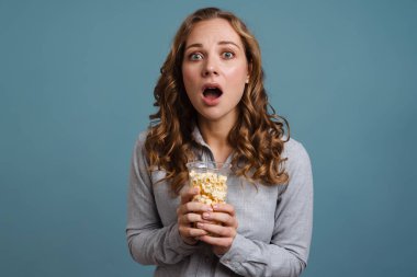 Mavi arka planda izlenmiş bir film izlerken patlamış mısır yiyen güzel bir kız.