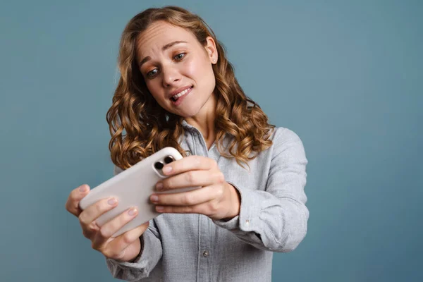 青の背景に隔離された携帯電話でゲームをプレイする幸せな若い女性の肖像画を閉じます — ストック写真