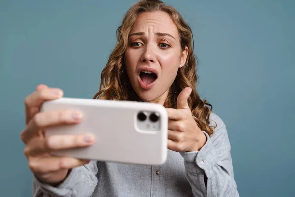 青の背景に隔離された携帯電話でゲームをプレイする幸せな若い女性の肖像画を閉じます — ストック写真