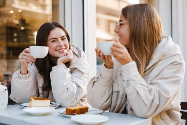 İki neşeli ve çekici bayan arkadaş kafeteryada çay içip kek yiyorlar.