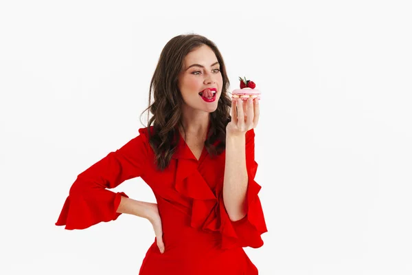 美しい赤のドレスの若い女性は 白い背景に隔離されたおいしいケーキを食べるしようとしました — ストック写真