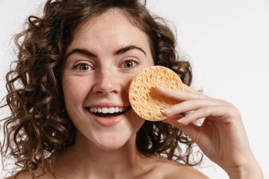 Beyaz arka planda izole edilmiş kozmetik süngerle poz veren mutlu üstsüz güzel kız.