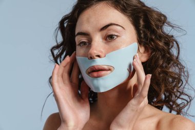 Güzel, yarı çıplak, maskesiyle poz veren güzel kız mavi arka planda izole edilmiş.