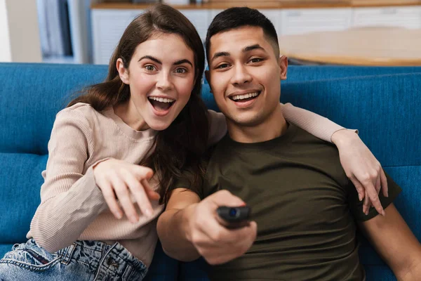 Szczęśliwa Młoda Para Siedzi Kanapie Ogląda Telewizję Salonie — Zdjęcie stockowe