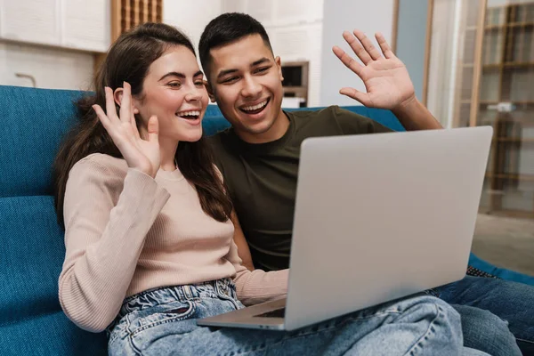 Uśmiechnięta Szczęśliwa Para Podczas Rozmowy Wideo Przez Laptop Siedząc Kanapie — Zdjęcie stockowe